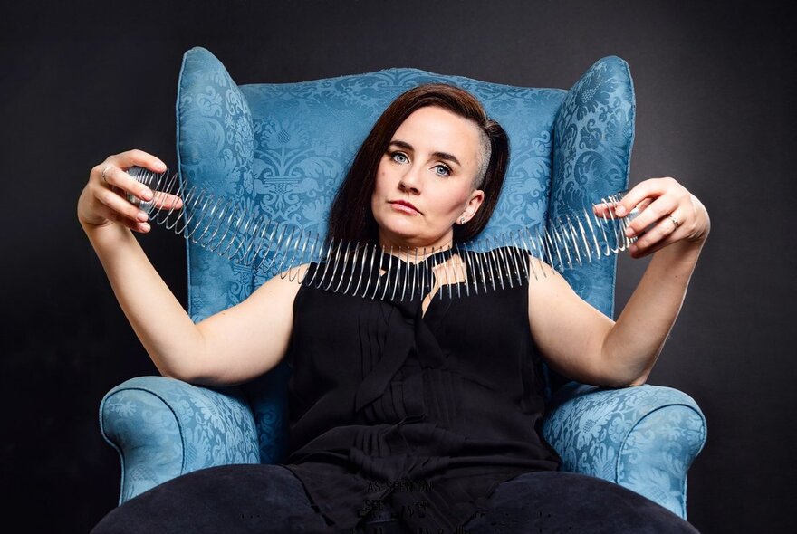 Woman with shaved side-parted hair, seated in a blue armchair, holding a slinky.