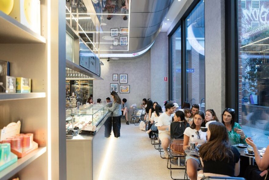 Sleek  interior of retail cafe space with people seated at tables eating food and drinks, a counter of food, and display areas showing collectible toys and objects.