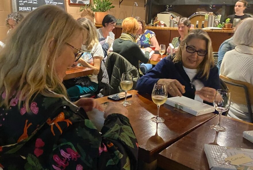 People seated at tables in a wine bar with glasses of wine and books.