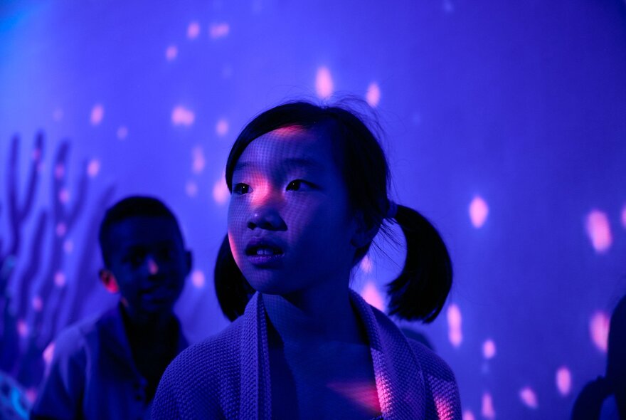 Two young children in a museum space that is coloured with a blue light, as if it under water.