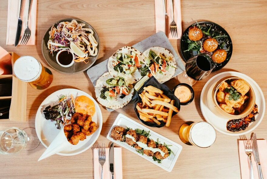 Overhead view looking down at a table of different shaped plates of food and drinks, and cutlery.