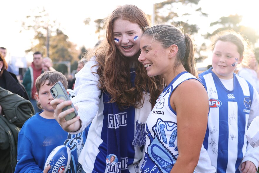 A North Melbourne AFLW player smiling for a selfie with fans. 