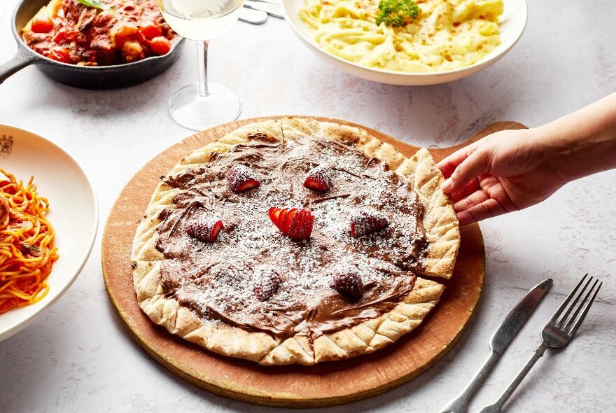 Table with dishes of pasta, a sweet pizza and cutlery.