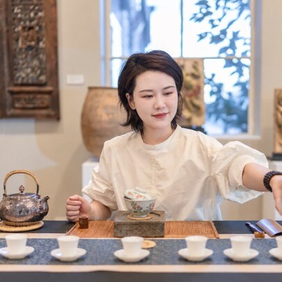 A person demonstrating a traditional Chinese tea ceremony behind a table set with small cups and a kettle.