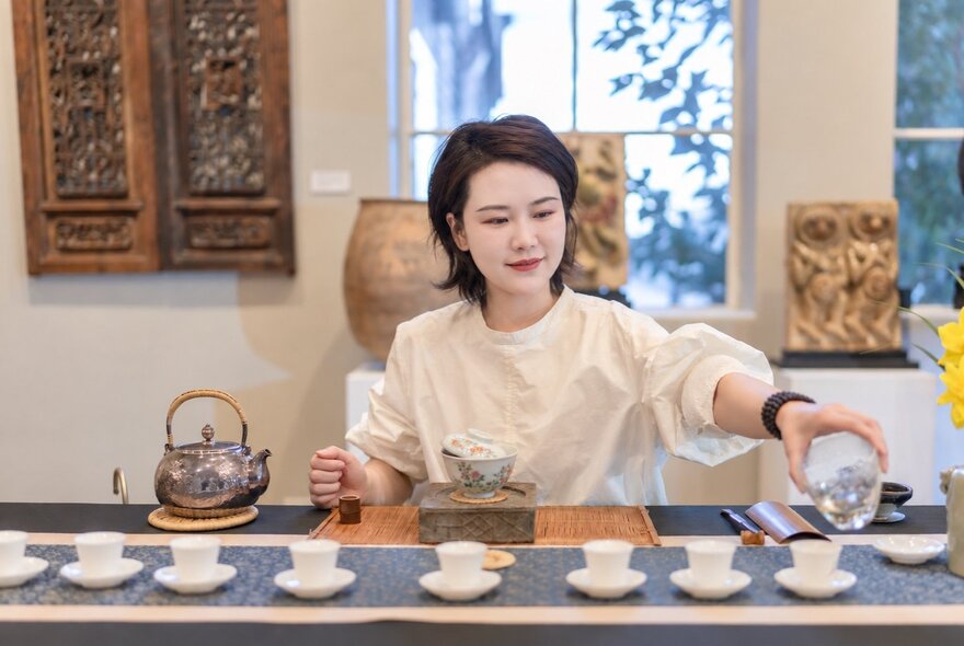 A person demonstrating a traditional Chinese tea ceremony behind a table set with small cups and a kettle.