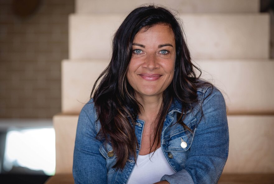 Alison Page, an Australian designer and curator, with dark hair and blue eyes, smiling at the camera, wearing a white shirt and a denim jacket.