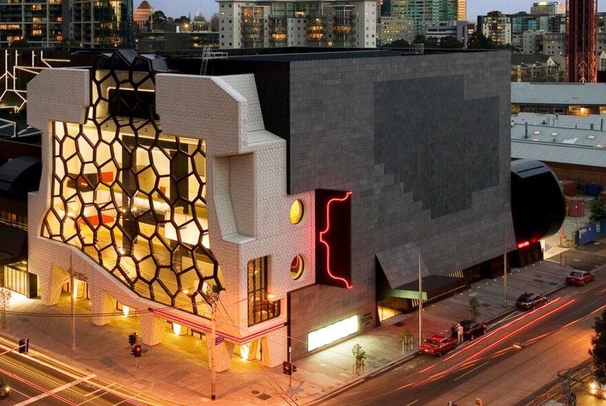 The illuminated honeycomb facade and side wall of the Melbourne Recital Centre building, on the corner of two busy city roads.