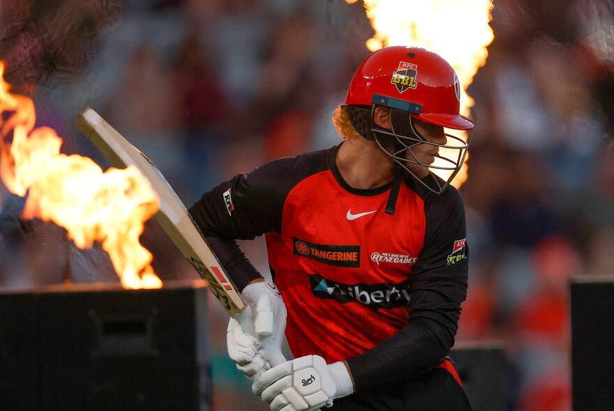 A Melbourne Renegades BBL player on the cricket field, holding a cricket bat, with flames in the background.