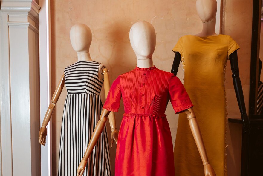 Three faceless mannequins wearing bold and brightly coloured dresses.