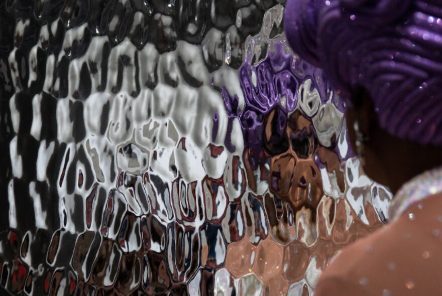 Thick textured glass reflecting a figure with purple hair. 