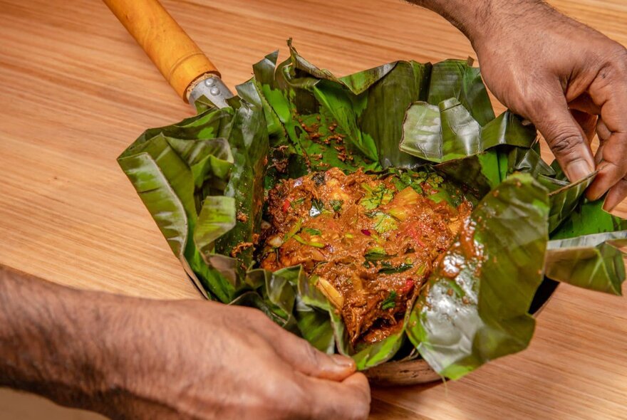 A pair of hands unpeeling the banana leaf casing of a special rice dish.