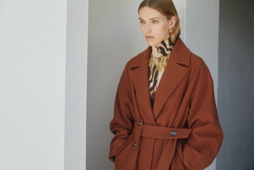 Woman in orangey-brown coat with patterned high-neck top underneath.