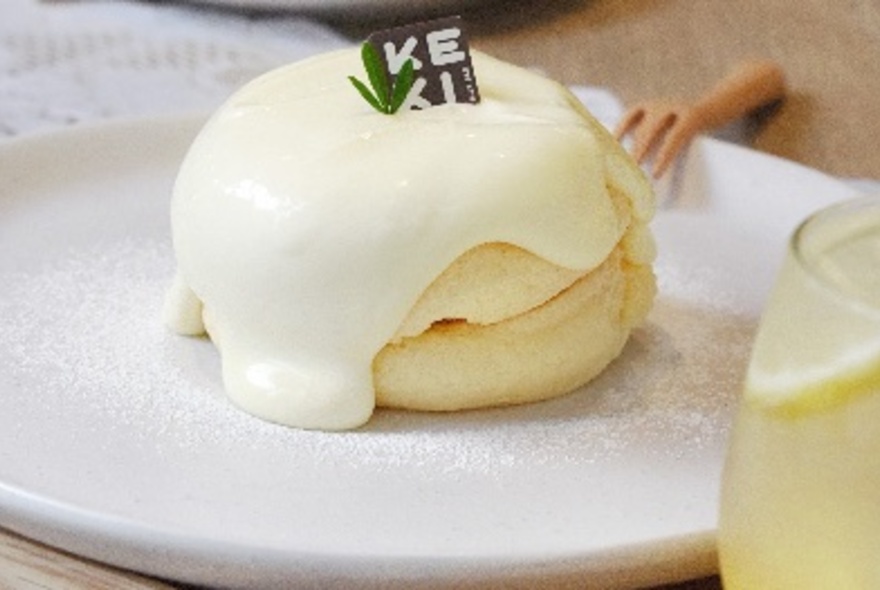 Two soufflé pancakes on a plate covered in custard cream.