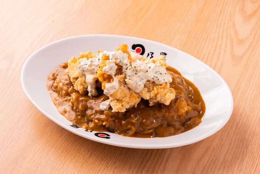 Japanese curry with fried chicken on top in a white bowl on a wooden surface.