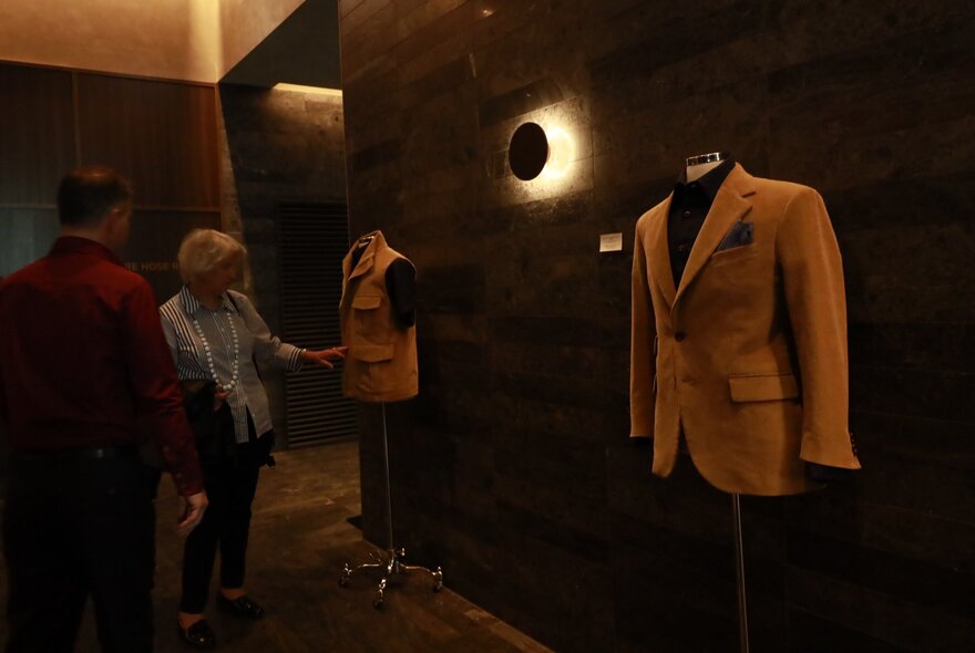 A tailored suit jacket displayed in a men's clothing store with two people looking and touching the garment.