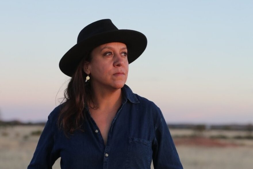Film-maker Rachel Perkins, wearing a black Akubra hat and a dark shirt, in a flat coastal landscape.