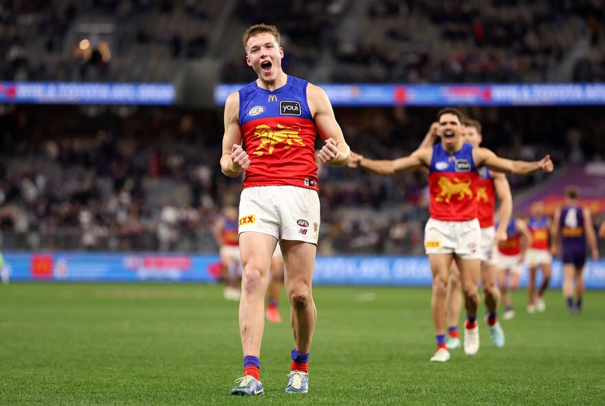 Brisbane Lions players celebrating on the football field while walking in a straight line. 