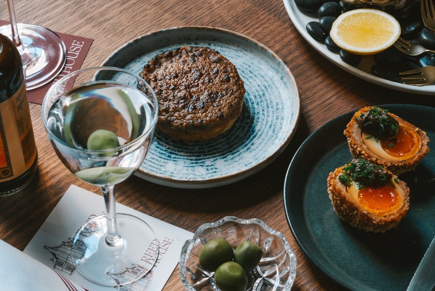 Plates showing a crumpet, scotch egg and olives, with a martini. 