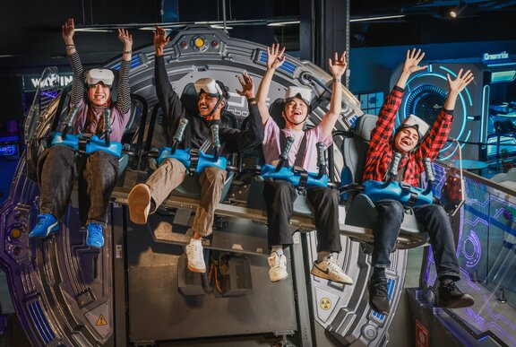 Four young people holding their arms up on a VR ride.