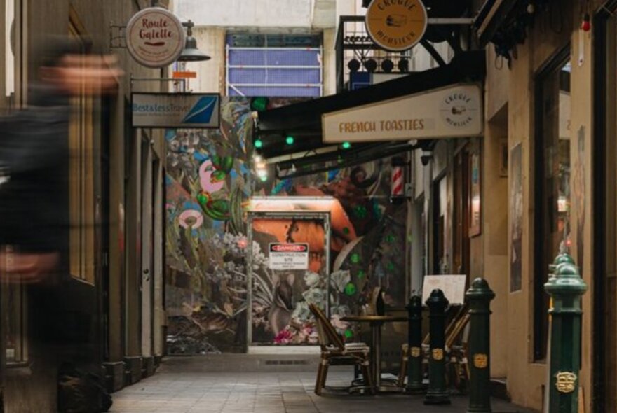 A laneway with cafes and a mural at the end.