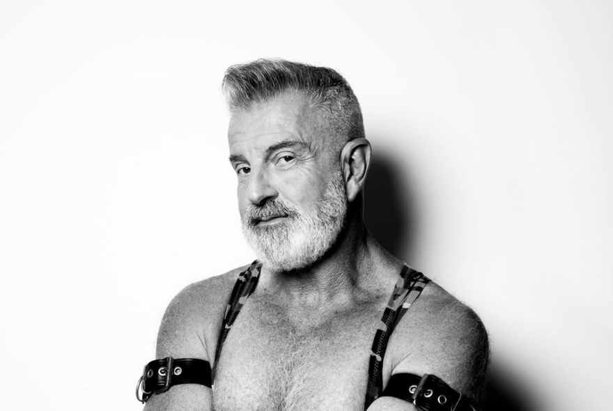 Black and white portrait of comedian, Brent Thorpe, from the chest up wearing straps over his shoulders and mini-belts around his upper arms.