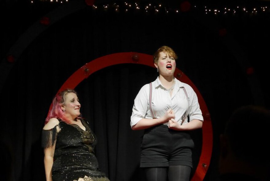 Two impro performers on a stage, one of them singing.