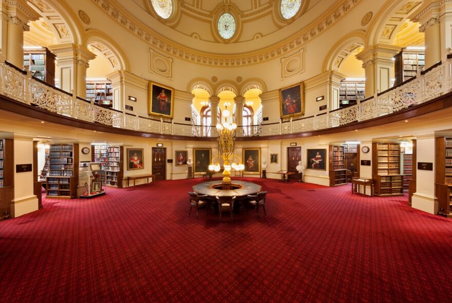 Historic Supreme Court Library interior with red carpet, arched mezzanine story, domed ceiling, stacks of library shelves and portraits.