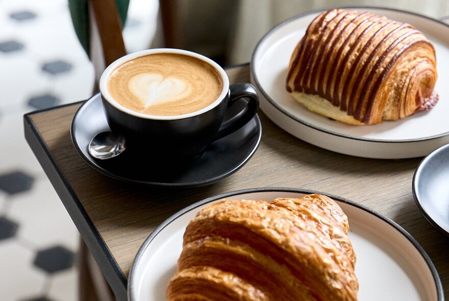 A table with two flaky pastries on plates, and a cup of coffee.