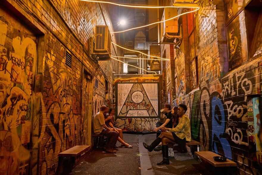 A group of friends are gathered outside a bar in a graffiti-covered laneway