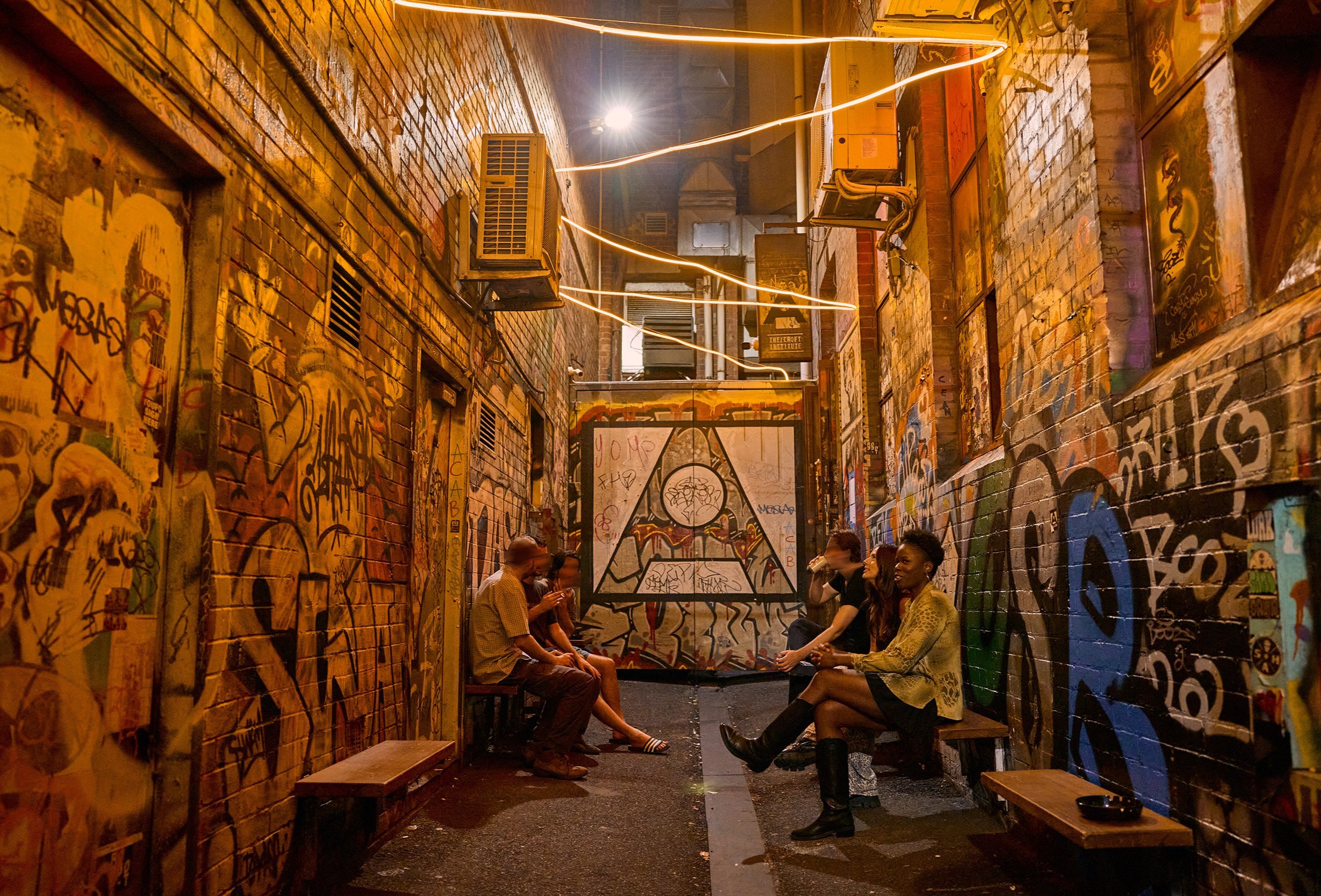 A group of friends are gathered outside a bar in a graffiti-covered laneway