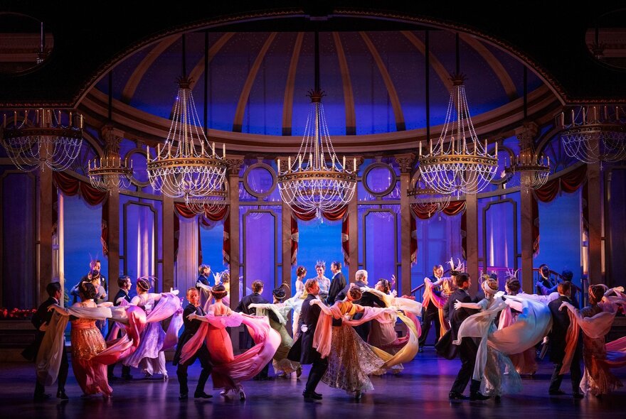 A scene from the musical My Fair Lady, with a large ensemble cast dancing on stage under chandeliers. 