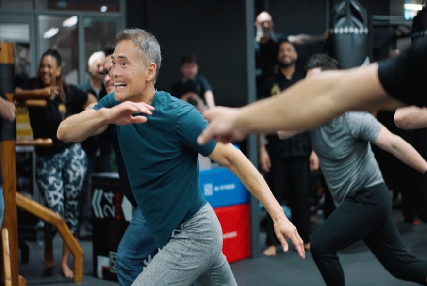 Martial-arts-based fitness class with participants lunging with arms outstretched.