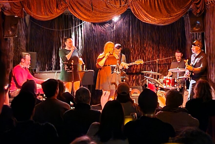 Band performing on a small stage to an audience.