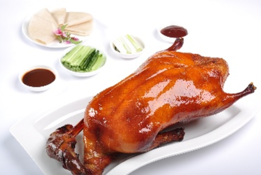 Glazed Peking cuk on a white platter with condiments.