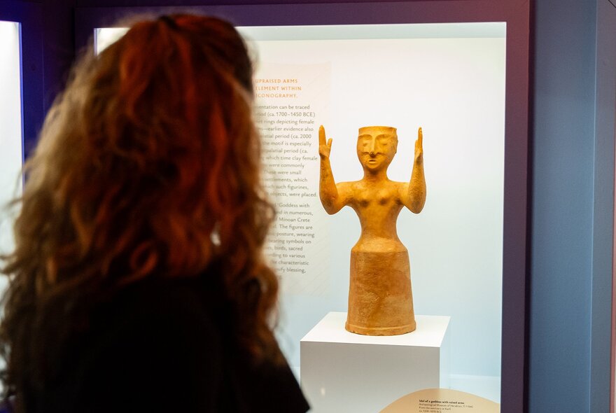 Person looking at an Archaic Greek statue of a woman raising her arms.
