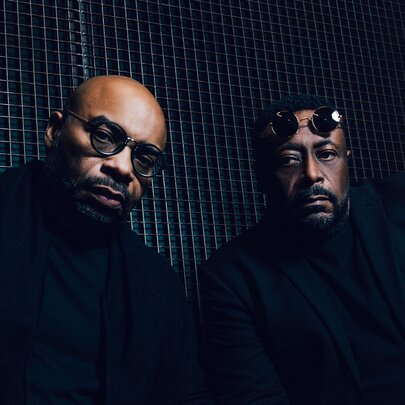 Two members of Octave One, a Detroit techno music group, both wearing black clothing and looking directly at the camera.