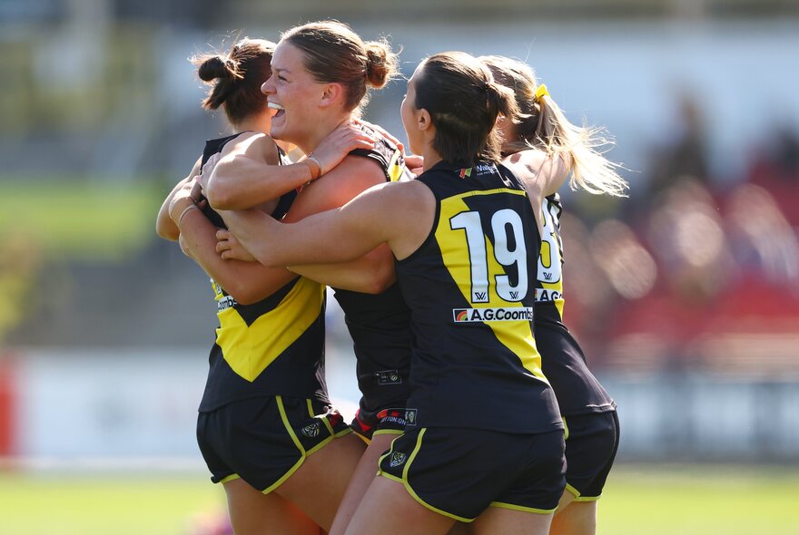 Richmond AFLW football players in a hug on the field.