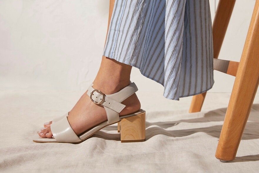 Detail of woman's leg with striped dress and beige sandals with buckles and heels.