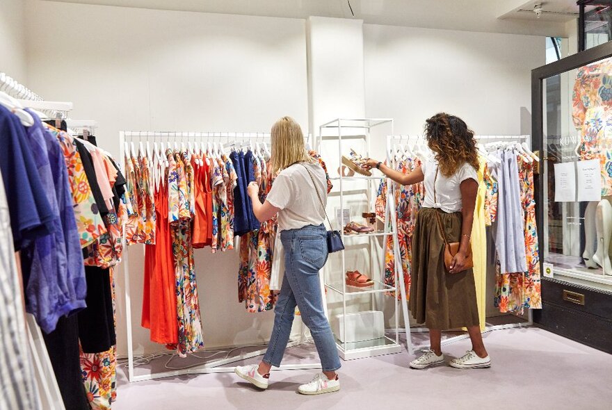 Two people browsing through racks of colourful summer clothing.