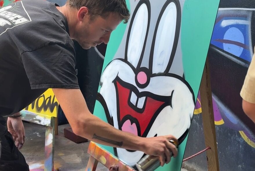 An artist using spray paint to create a large cartoon artwork.
