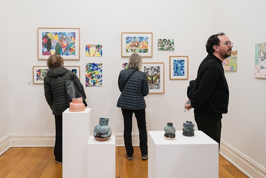Three people looking at different artwork hanging in a gallery space. 
