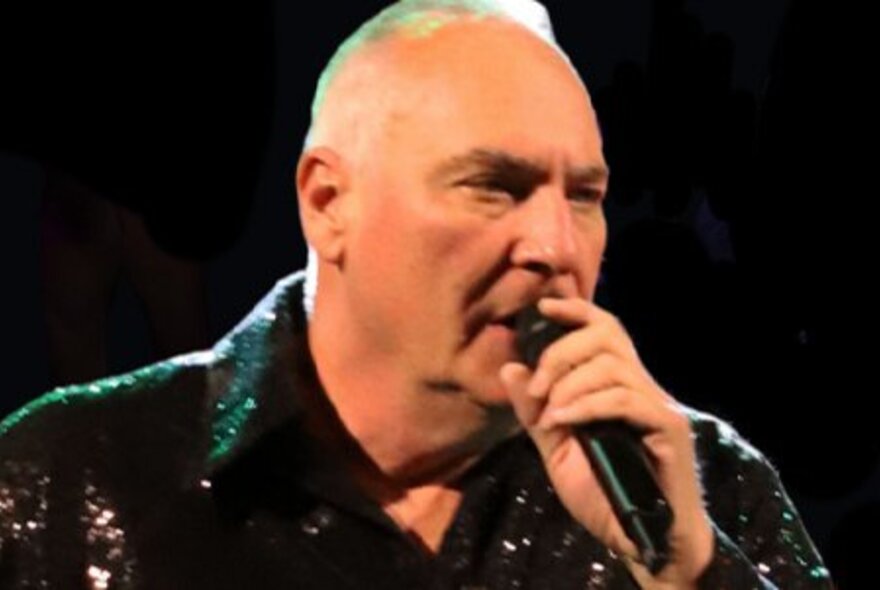 Male singer Jason Taylor singing into a microphone in a Neil Diamond tribute band.