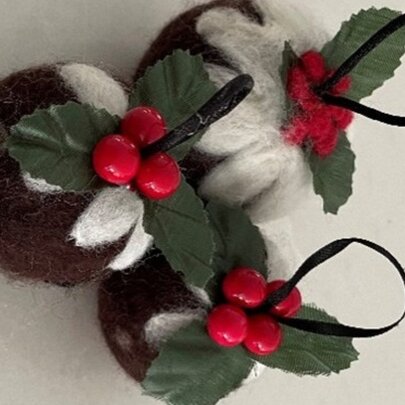 Felted festive Christmas pudding ornaments are crafted from handmade wool felt with green leaves with bright red holly berries.