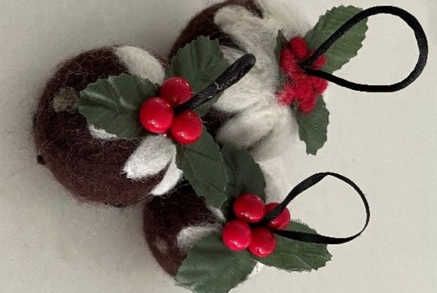 Felted festive Christmas pudding ornaments are crafted from handmade wool felt with green leaves with bright red holly berries.
