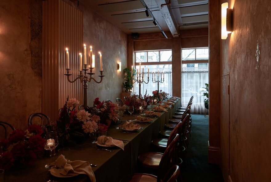 Long table inside a restaurant venue, set with candelabras flowers and a dinner setting, as if for an event.