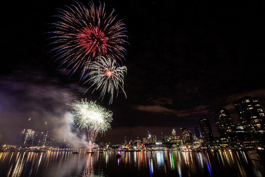 Nighttime with Yarra River in foreground and illuminated banks of city skyline in background with firework displays.