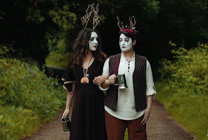 A couple wearing white makeup with black tears and crowns, standing outside.