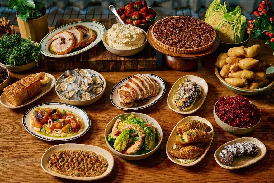 Several platters of food on a wooden table.