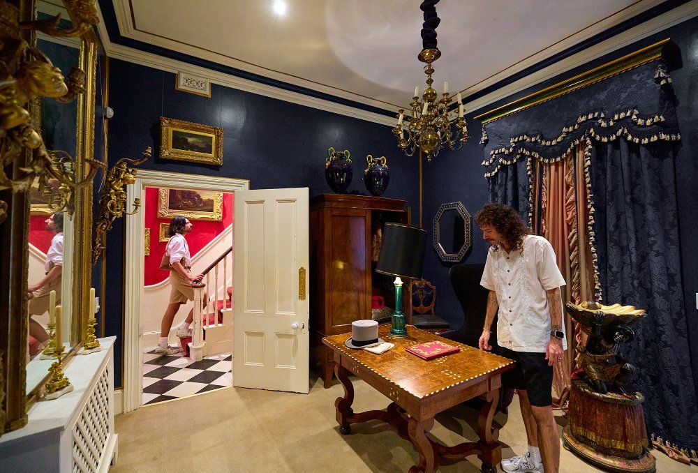 Two men exploring a house filled with antiques.
