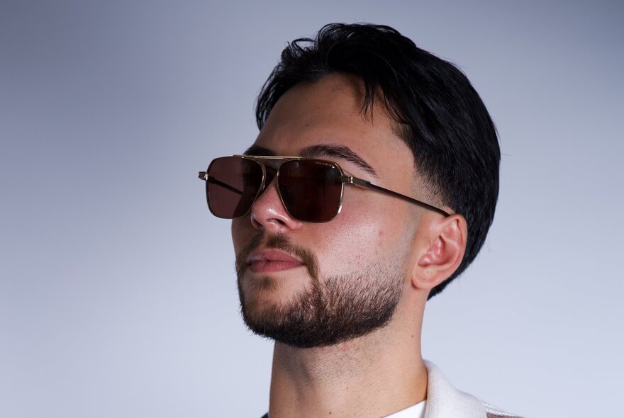 A young man's head in side profile, with a short beard and dark hair, wearing sunglasses.